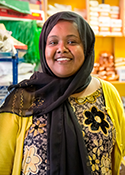 Deeqo Jibril wears a bright yellow cardigan and stands in a store