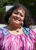 A Hispanic woman wearing a colorful tie-dye shirt stands outside