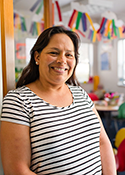 Maria Elvia Salazar wears a striped shirt and stands in front of a table