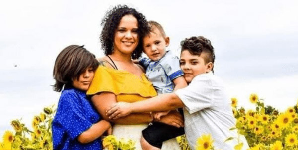 A mother carries one of her children and her other two children hug her tightly