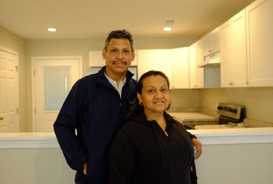 A hispanic couple stands in front of the kitchen of their new shared equity home