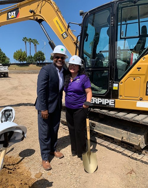 Sean Spear stands with a member of the community in front of a CAT machine for a groundbreaking to build more affordable homes