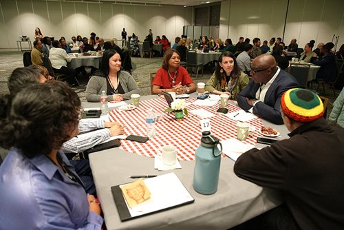 Attendees at NeighborWorks America's symposium sit around a table styled like a kitchen table, meant to evoke the deep, personal conversations that take place there