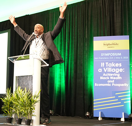 Pastor Daniels at NeighborWorks America's symposium raises his hands on the stage