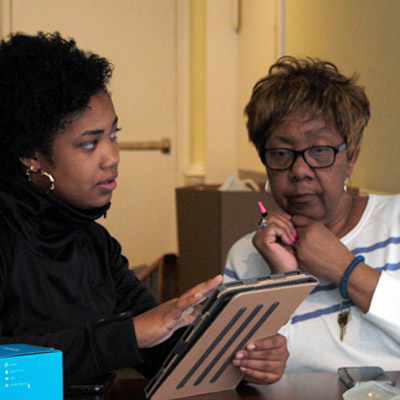 A volunteer sits with an older adult to teach her how to use the Amazon Echo Dot