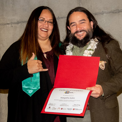 A man and a woman wearing dark clothes hold a diploma