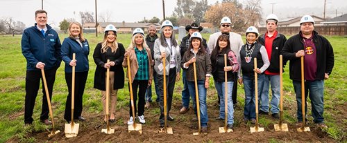 The community stands ready to break ground. Thirteen people hold shovels.