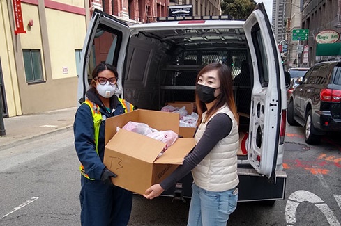 Two women stand outside a van, ready to distribute food.