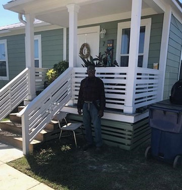 Johnny Carter stands outside his new home, which is white and green and has a small front porch.