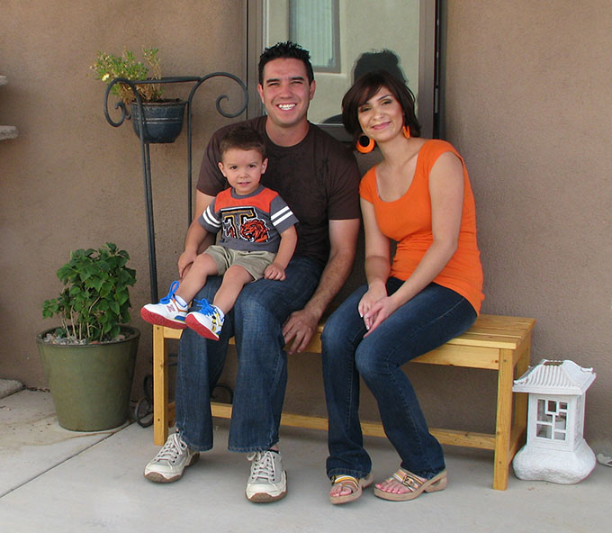 A Latinx family sits in front of their new home in New Mexico