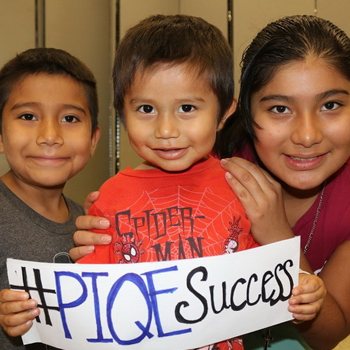 Three Latino children hold up a sign that says #PIQESuccess