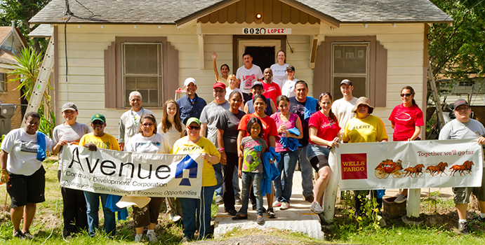 A mixed group of people stand in front of a beige house