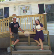 A VISTA member stands next to a member of the community on the porch outside of his manufactured home