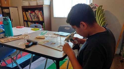 A student works on a project while receiving afternoon tutoring. In front of him is a model made of tooth picks.