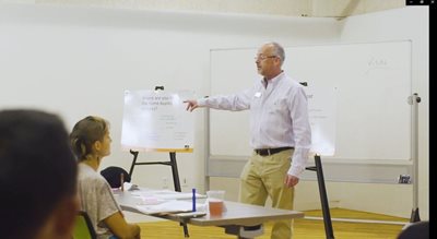 Kenneth Brown instructs a class on home buying. He stands at the front of the room, while students listen.