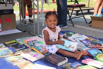 A girl sits and reads at the backpack distribution for Lawrence Community Works.