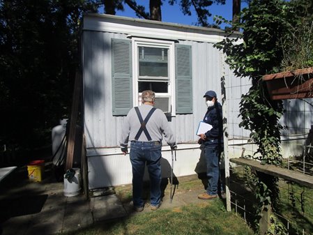 Two men stand outside an outdoor A/C unit to help weatherize a home