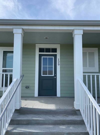 A close-up of one of the homes int eh complex shows pale green siding and a front porch.