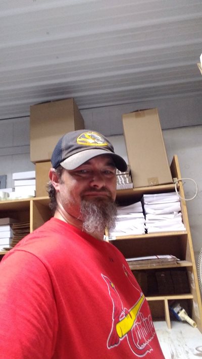 Eric Nokes smiles in a red shirt and in front of a bunch of boxes.