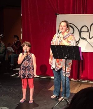 Jenn Lamb with her daughter, Izzy, stand in front of a microphone.