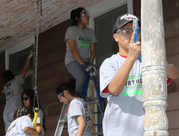 A gruop of people help renovate a home by repainting it and repairing the porch