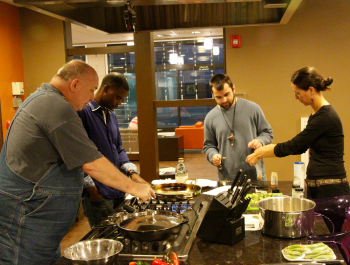 A group of people standing in a kitchen preparing food.