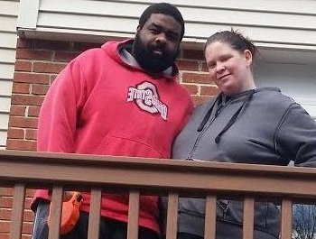 A black man and a white woman stand on the porch of their new home