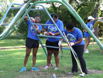 Three women re-paint a slide in the community park