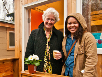 An older white woman and a younger black woman stand in front of a tiny home