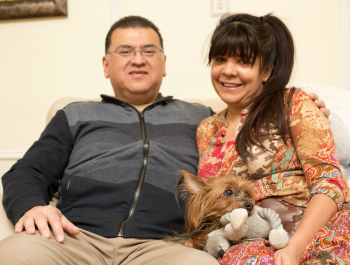 New homeowners Richard and Jacqueline sit on their couch holding a small dog.