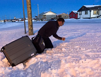 A white man carries his gray suitcase through four feet of snow in Alaska