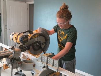 A girl cutting wood with an electric saw.