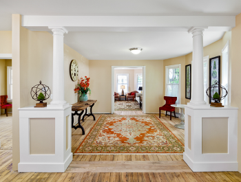 A renovated home with light wood floors, white walls and a flower-covered rug in the middle of the living room.