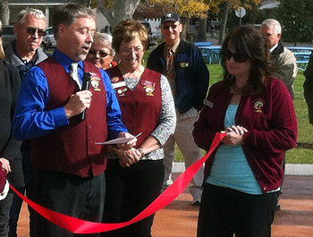 A man wearing a red vest and blue shirt speaks to a crowd at a ribbon cutting