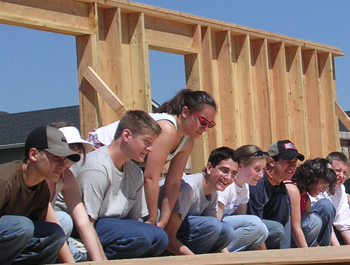 A mixed group of students work on building a house