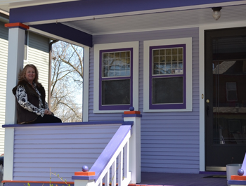 A white woman sits on the porch of her newly revitalized home