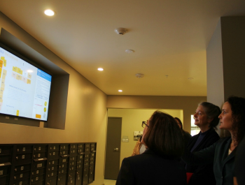 A group of people standing a watching a presentation being displayed on a screen.