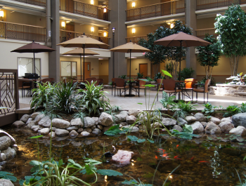 An indoor area with tables covered by umbrellas and a fountain with rocks and plants.