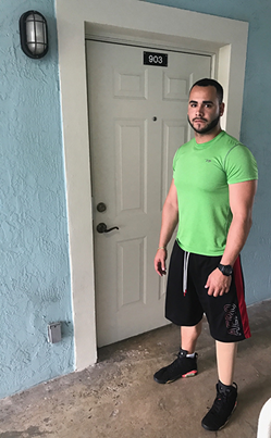 A disabled man wearing a green shirt and black track pants stands in front of his new home