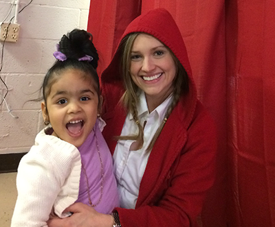 A girl sitting next to a woman wearing a red hood grins at the camera